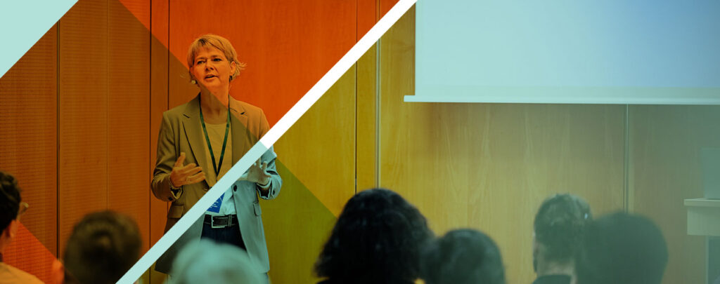 a woman with short blonde hair, speaking to a room of people in a conference room setting.