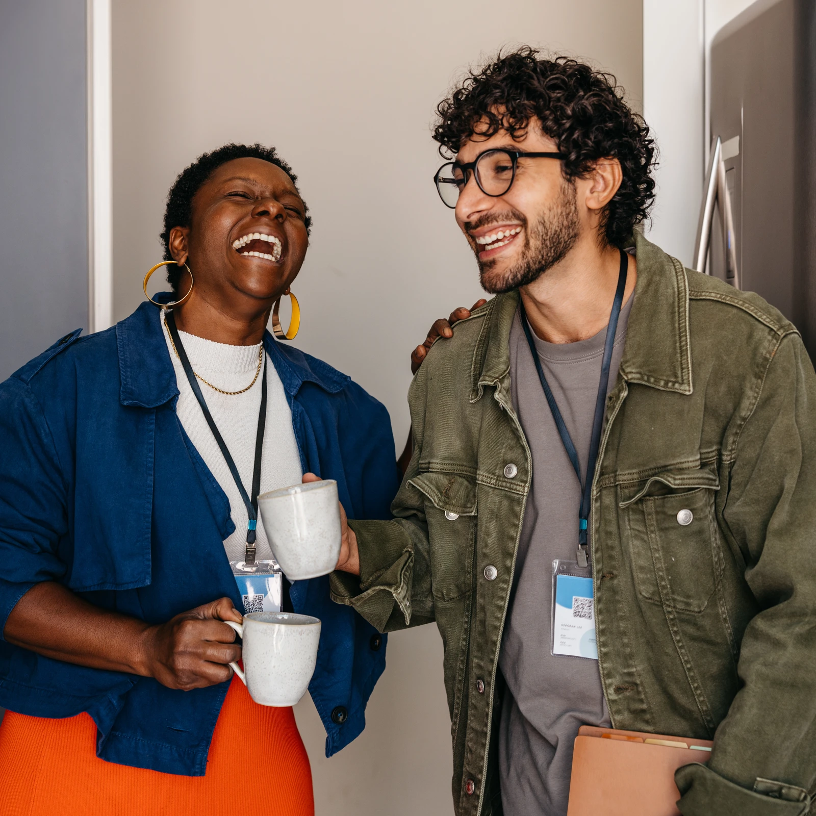 A photograph of two diverse corporate colleagues laughing warmly together over coffee, framed in a circular layout by Ingenuity Design.