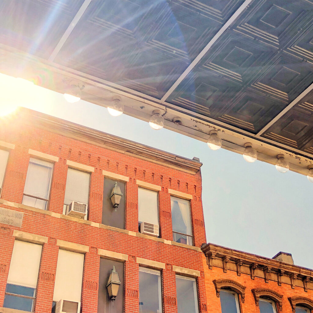 A low-angle, upward view of a classic brick building facade with sun rays gleaming over the roofline.
