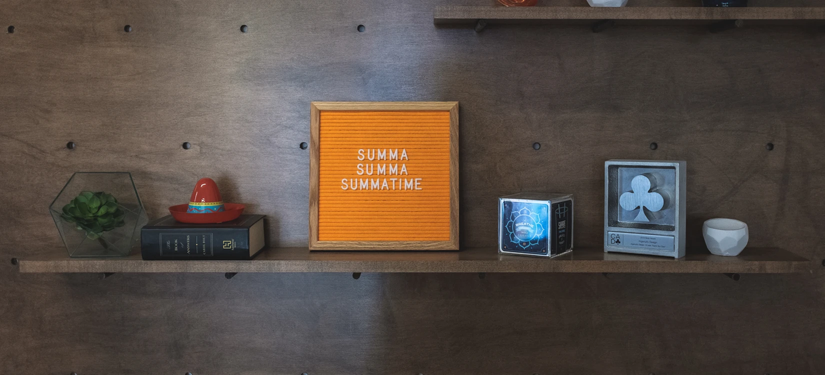 A neatly arranged display shelf from the former Ingenuity office, featuring a design award and an orange letter board that says "Summa, Summa, Summatime".