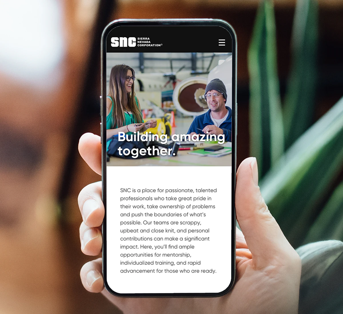 A hand holding a smartphone displaying a responsive mobile recruitment page with the header building amazing together.