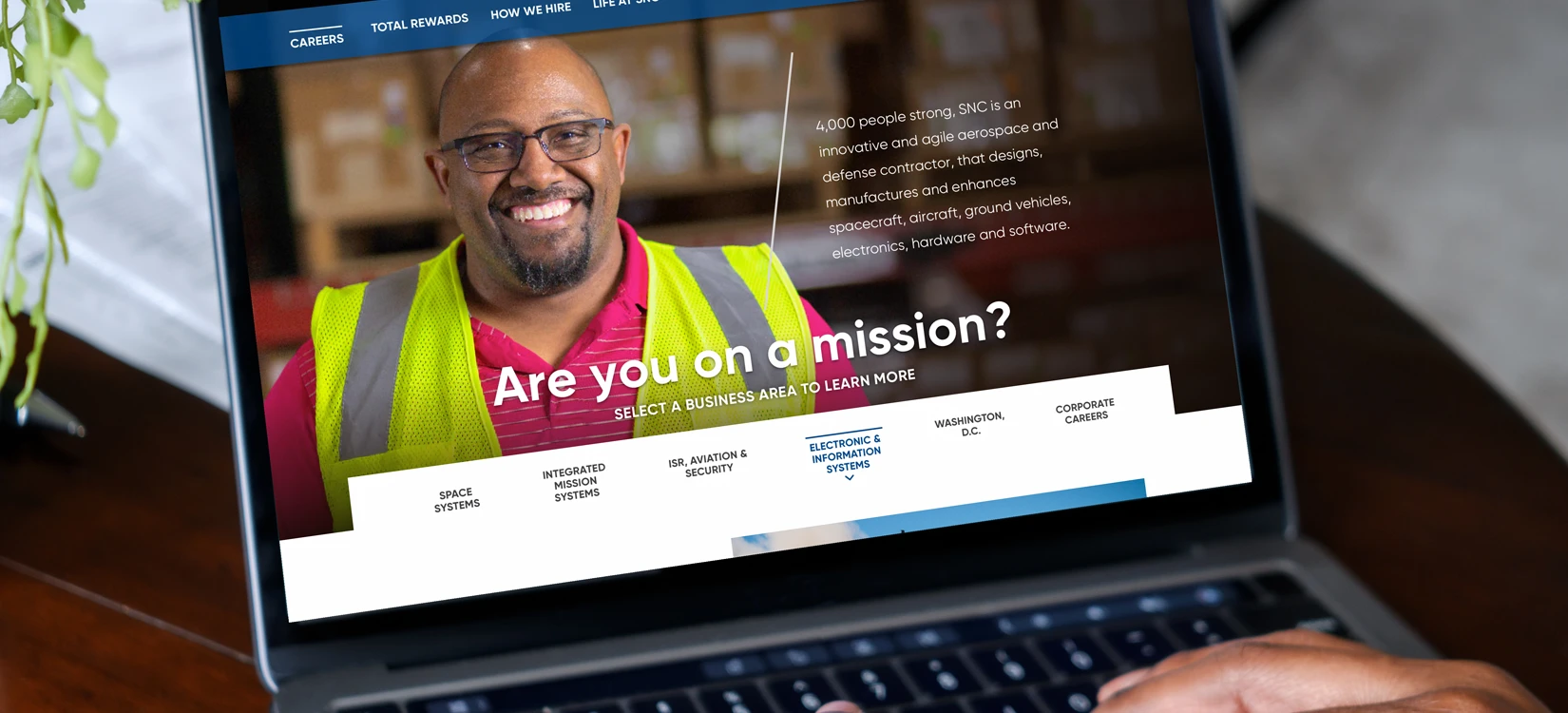 A laptop displaying a modern career site redesign featuring a smiling SNC worker in a high-visibility vest.