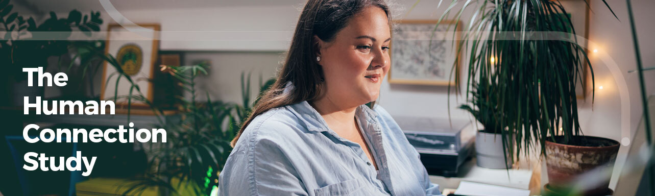 A woman sandy blonde woman working in a home office on a laptop. She's smiling and is wearing a chambray blue button down collared shirt